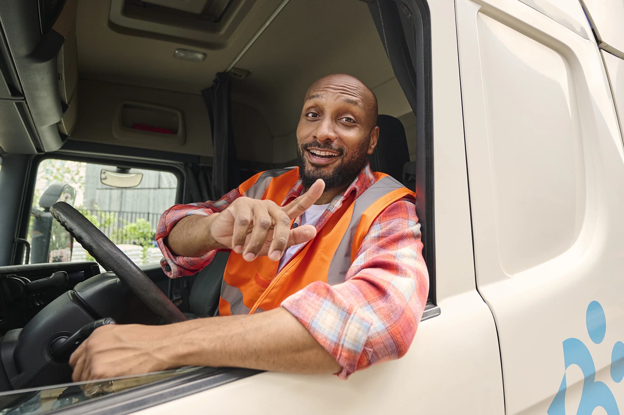 Șofer de camion cu vestă reflectorizantă zâmbește și arată din cabină — joburi în transport prin Accent